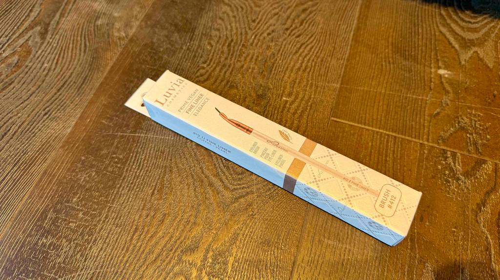 Ein getesteter Eyeliner-Pinsel liegt in seiner Verpackung auf einem Holzuntergrund.