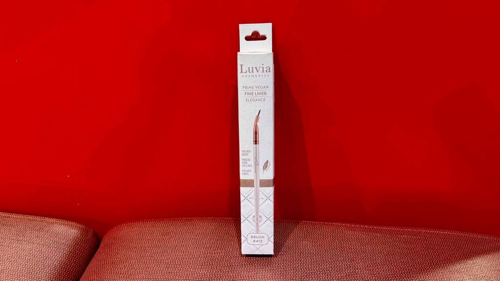Ein getesteter Eyeliner-Pinsel steht in seiner Verpackung vor einem roten Hintzergrund.