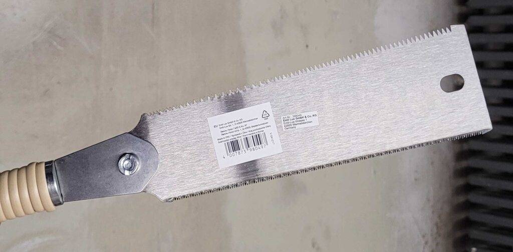 Nahaufnahme des Sägeblatts einer getesteten Ryoba-Säge inklusive Barcode vor einem Zementboden.