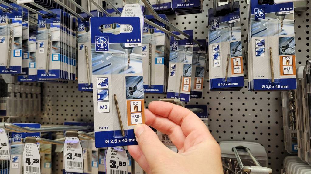 Edelstahlbohrer-Test: Ansicht auf den Bohrer M3 inklusive Verpackung von Lux-Tools in einer Hand vor einem Verkaufsregal.