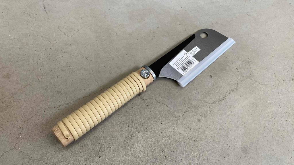 Im Test: Japansäge von Lux Tools liegt schräg mit Stiel nach unten links auf Betonboden.