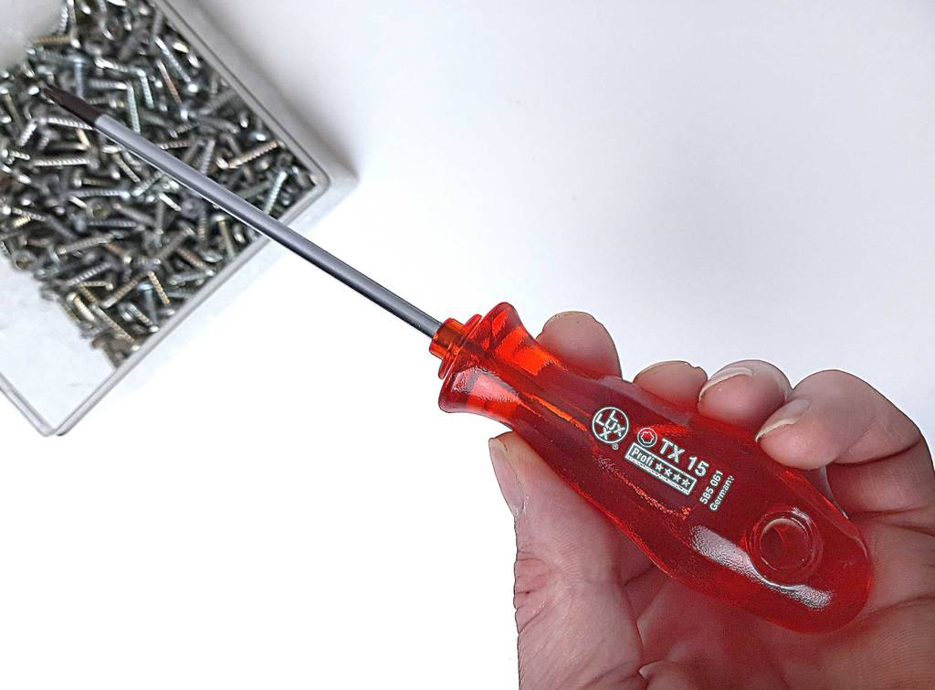 Schraubendreher im Test: Ein Modell mit rotem Griff in einer Hand über einer Dose mit Schrauben.