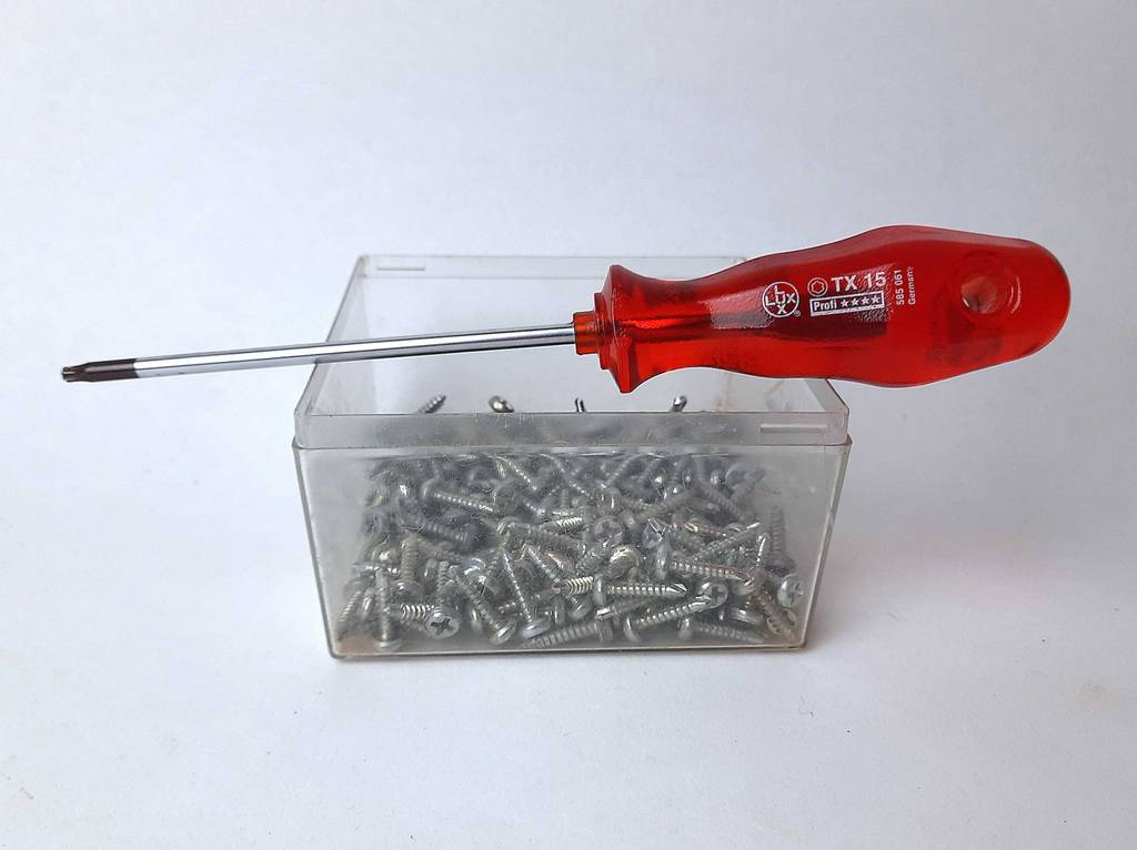 Schraubendreher im Test: Ein Modell mit rotem Griff liegt auf einer Dose mit Schrauben.