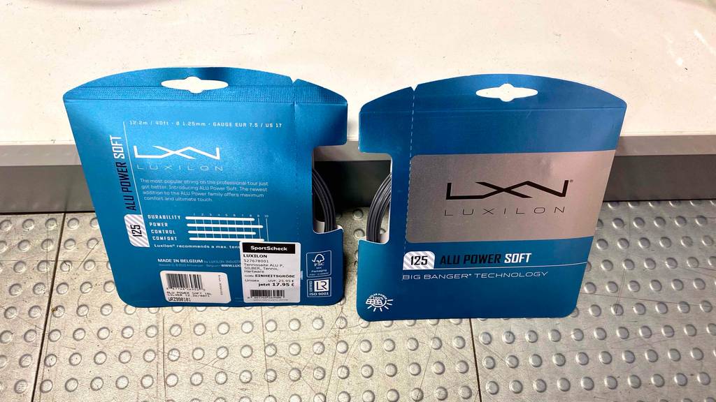 Tennissaiten-Test: zwei blaue Packungen inklusive Tennissaiten von Luxilon, eine mit der Vorder- und die andere mit der Rückseite stehen an der Wand gelehnt.