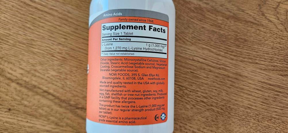 Auf einer Holzoberfläche befindet sich eine Verpackung von getesteten Lysin-Tabletten mit Nährwertangaben.