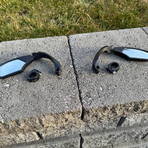 Die M-Wave-SPY-Space-Fahrradspiegel in Schwarz liegen neben den Halterungen auf einem Stein.