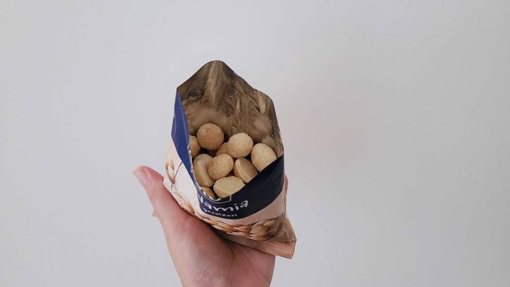 Eine Hand hält eine geöffnete Packung Macadamia-Nüsse im Test nach oben vor eine helle Fläche.