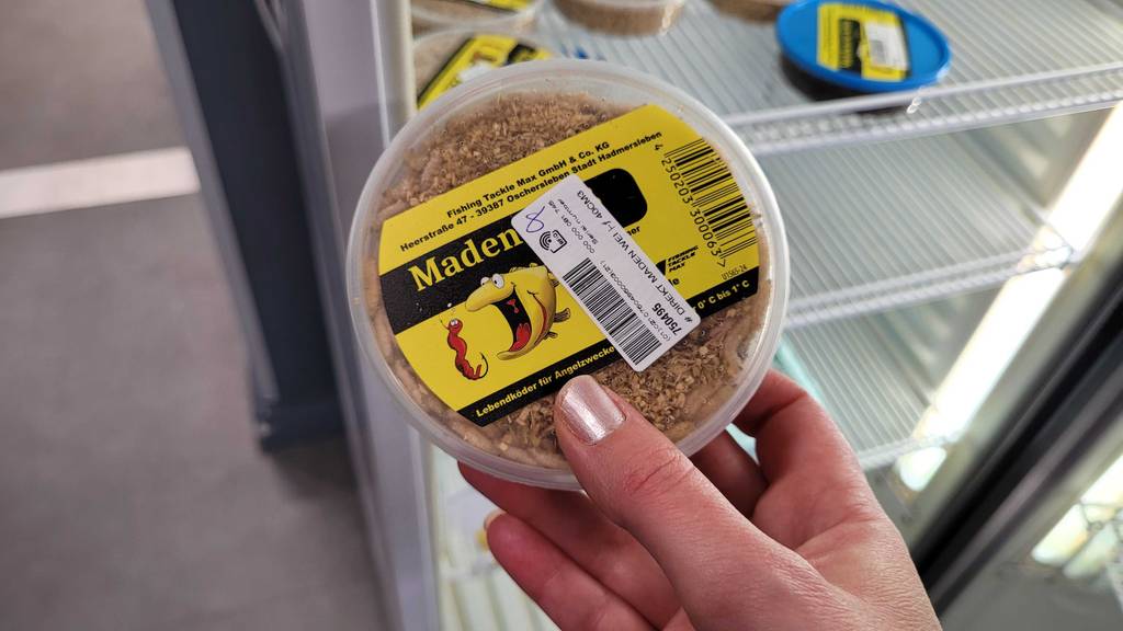 Eine Hand hält eine Dose Angelköder zum Testen.