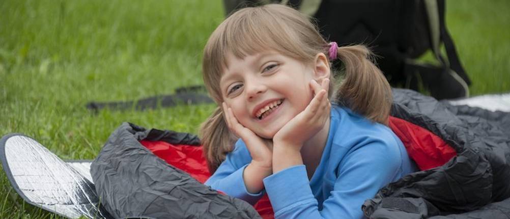 Kinderschlafsack-Test: Ein im Schlafsack liegendes Mädchen auf einer Wiese.