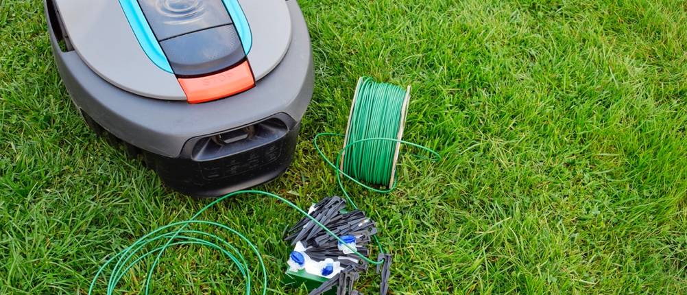 Ein Mähroboter mit daneben liegendem Begrenzungskabel, das seinen Radius limitiert.