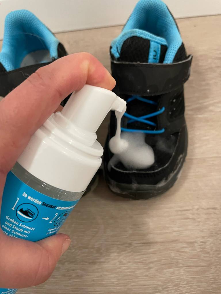 Ein Finger drückt auf den Sprühknopf einer Dose Sneaker-Cleaner im Test und sprüht Schaum auf einen Schuh.