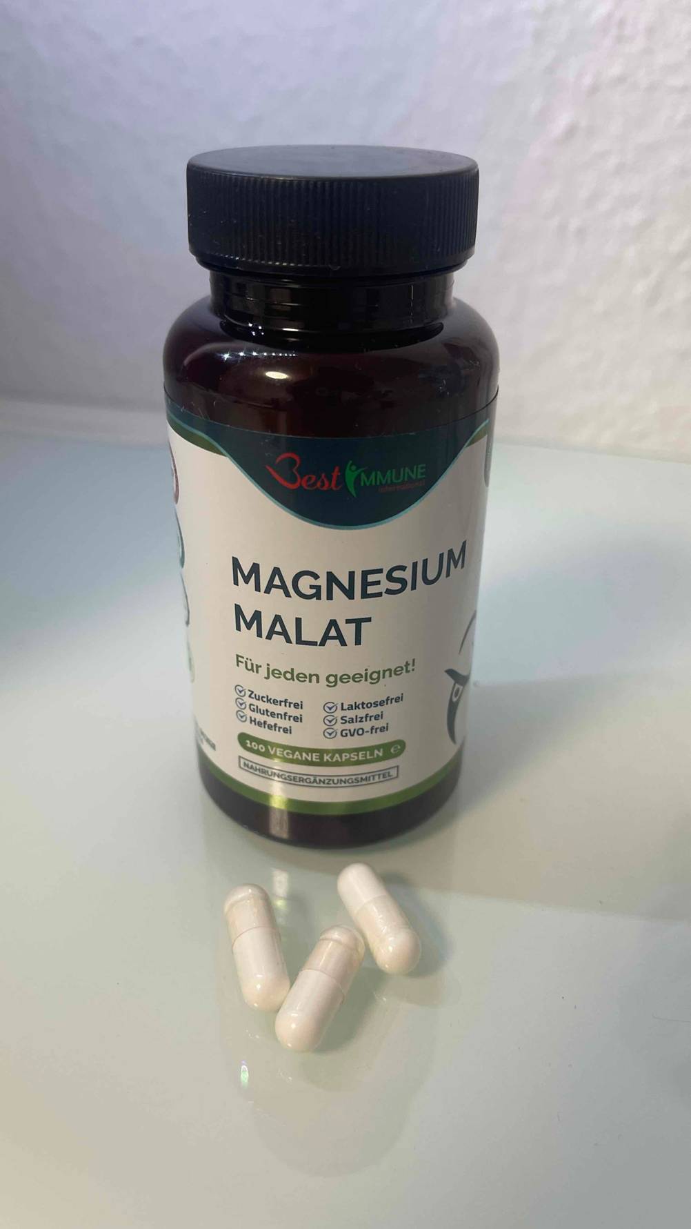 Das getestete Magnesium-Malat liegt in Form von drei weißen Kapseln vor der lichtdichten Schraubdose, die vor einer weißen Wand steht.