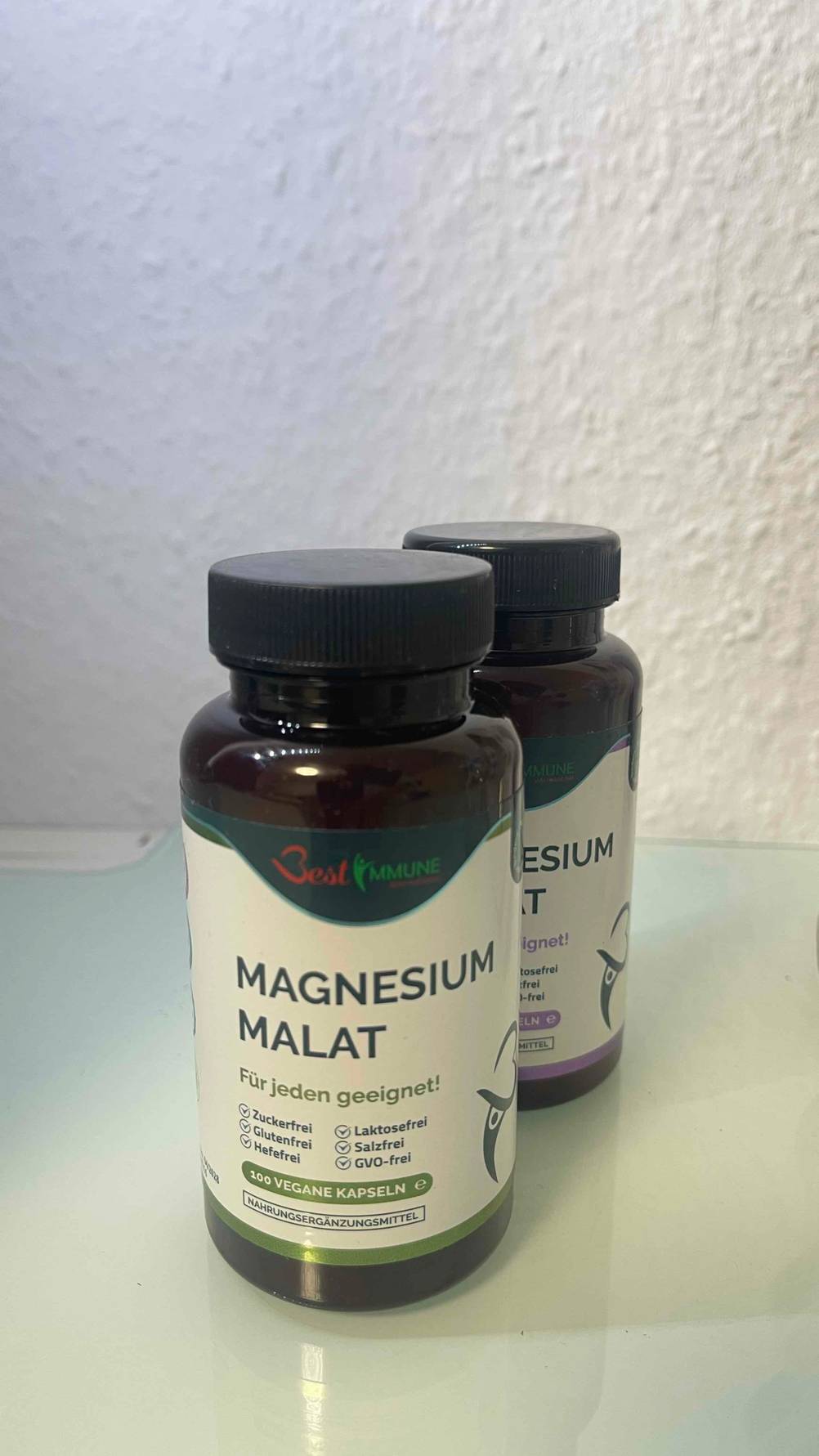 Im Test: Das Magnesium-Malat steht in zwei verschiedenen Varianten mit 100 veganen Kapseln in lichtdichten Schraubdosen vor einer weißen Wand.