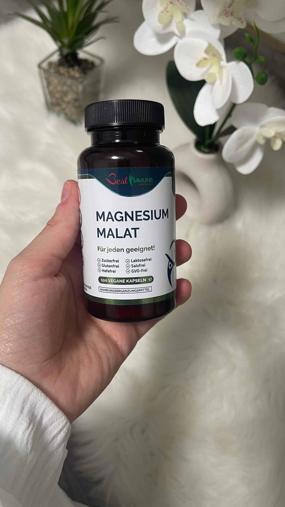 Eine Hand hält die Schraubdose mit dem getesteten Magnesium-Malat über einer weißen Oberfläche.