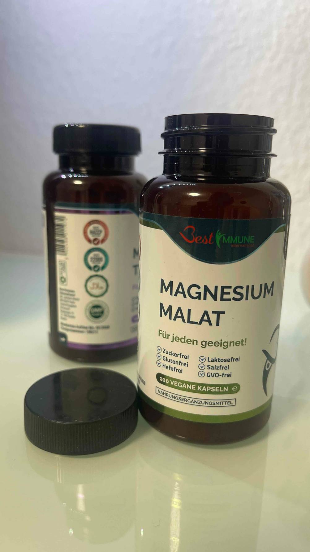 Das für jeden geeignete, getestete Magnesium-Malat befindet sich in zwei verschiedenen lichtdichten Schraubdosen vor einer weißen Wand.