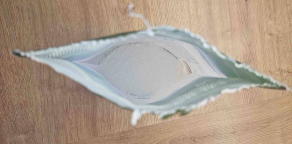 Nahaufnahme von oben auf einen weißen, wiederverschließbaren Standbeutel inklusive getestetem, hoch dosierten Magnesium-Pulver auf einem Holzuntergrund.