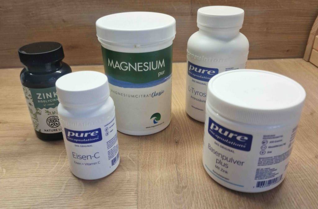 Hoch dosiertes Magnesium im Test: mehrere Produkte in Pulver- und Kapselform befinden sich in ihren weißen Verpackungsdosen auf einer Holzfläche.