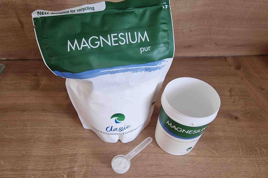 Im Test: Nachfüllpackung und Dose mit Dosierlöffel von Magnesiumcitrat Pulver steht auf Holzfläche.