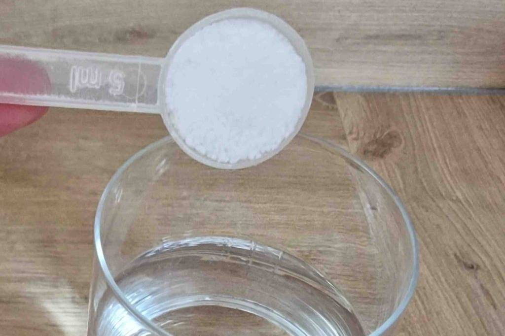 Im Test: Magnesiumcitrat Pulver wird mit Dosierlöffel in ein Glas Wasser gegeben.