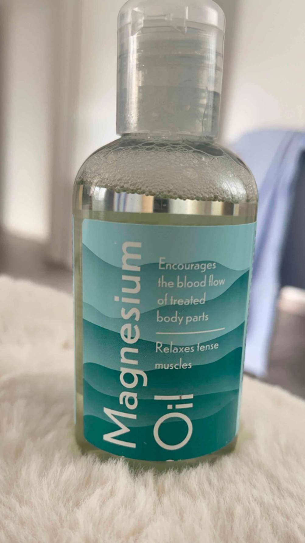 Getestet: Das Magnesiumöl steht innerhalb einer transparenten Flasche mit Dosierverschluss auf einem weißen Kunstfell.