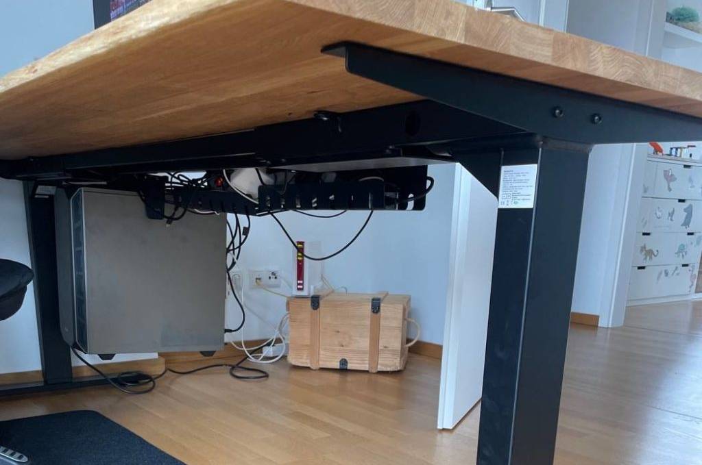 Höhenverstellbarer Schreibtisch im Test mit schwarzem Gestell und Holzplatte steht in einem Bürobereich auf Parkettboden.