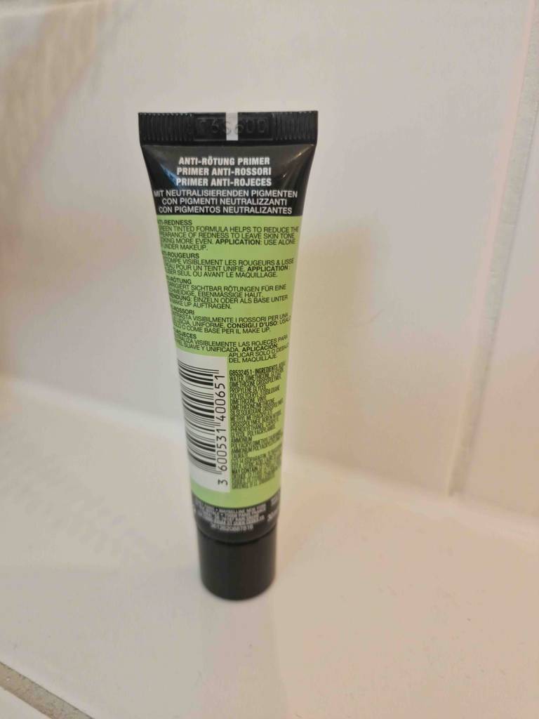 Ansicht der Rückseite inklusive Produktinformationen einer grün-schwarzen Tube Make-up-Primer im Test vor beigefarbenem Hintergrund.
