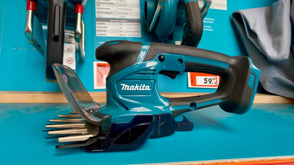 Im Test: Eine Akku-Grasschere von der Seite auf einem blauen Verkaufsregal. Im Hintergrund Preisschilder und andere Produkte.