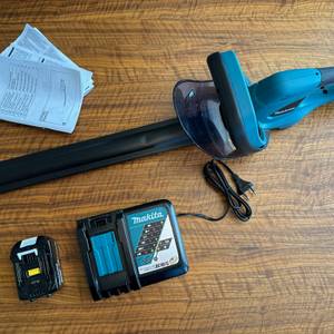 Die Makita DUH523Z liegt neben dem Akku, Ladegerät und den Anleitungen auf einem Tisch.