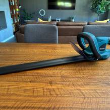 Die Makita DUH523Z liegt mit einem Schutz über dem Scherblatt auf einem Tisch.