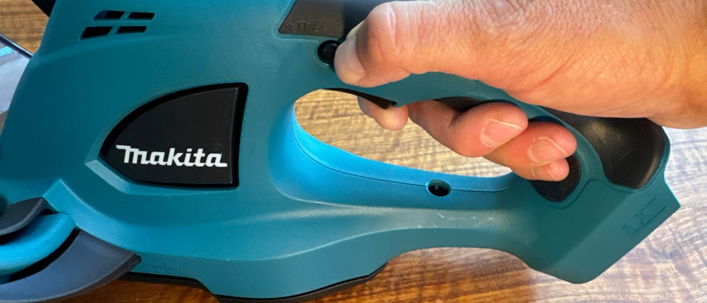 Eine Hand drückt die Sicherung der Makita DUH523Z.