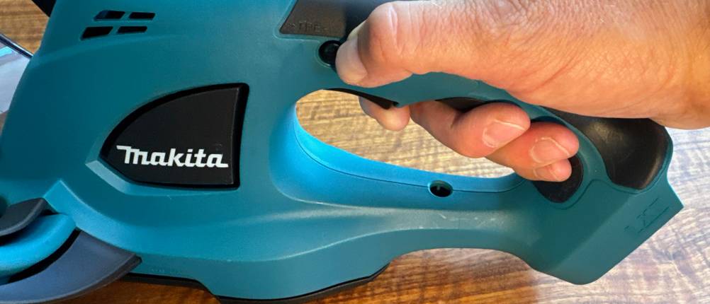 Eine Hand drückt die Sicherung der Makita DUH523Z.