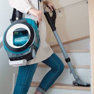 Eine Frau reinigt mit Trage-Staubsauger die Stufen einer Treppe.
