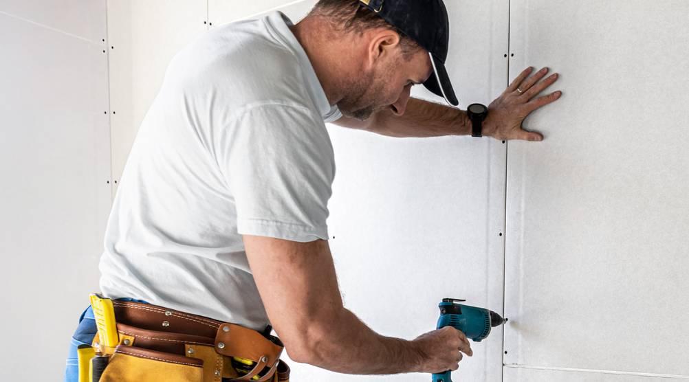 Makita-Trockenbauschrauber im Test Ein Mann schraubt an einer Gipskartonplatte mit einem kleinen Trockenbauschrauber.