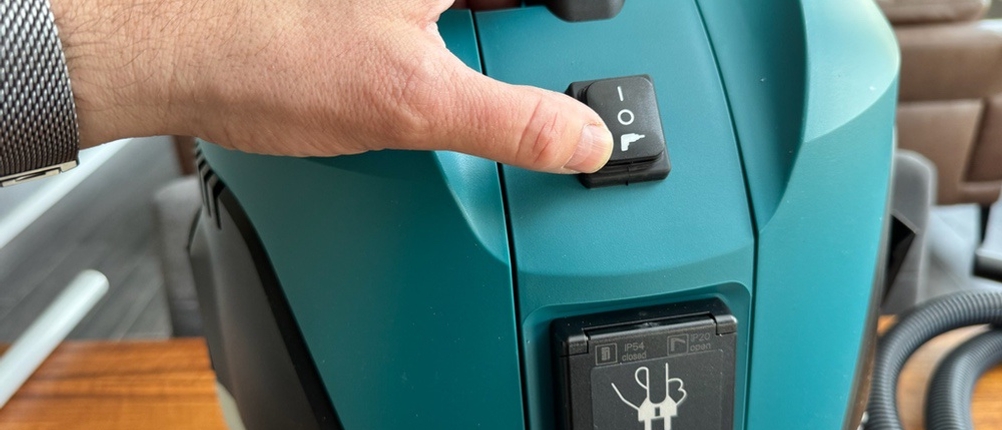 Eine Hand betätigt einen Knopf auf dem Makita VC2512L