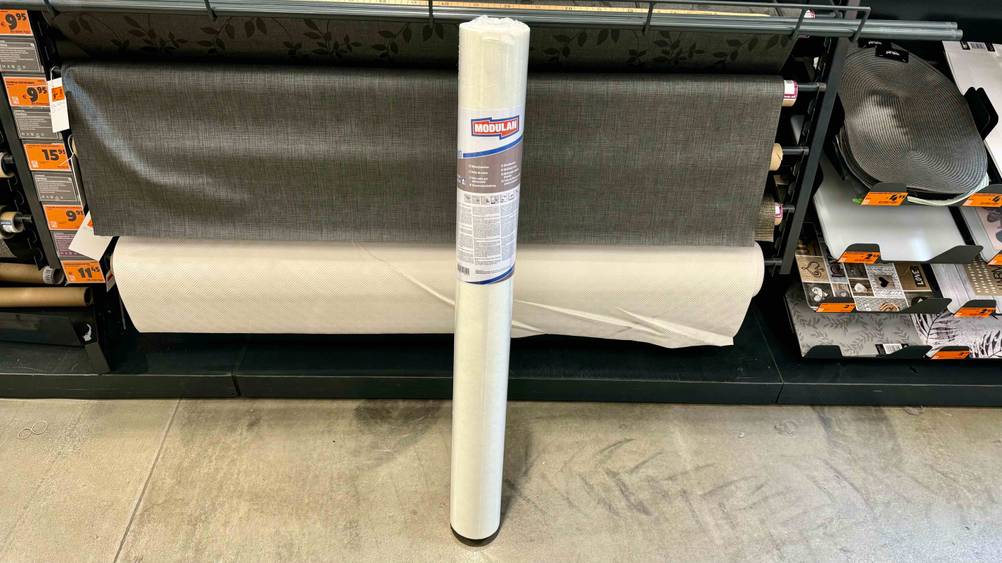 Eine Rolle der getesteten Malervlies-Tapete in einem Baumarkt im Hintergrund andere Produkte.