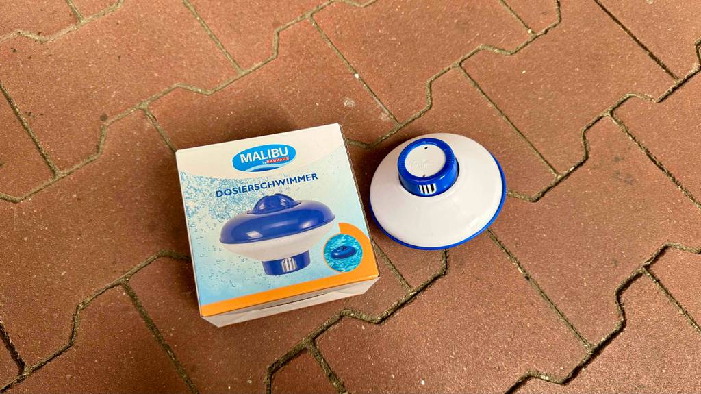 Ein getesteter Dosierschwimmer liegt mit der Unterseite nach oben neben der Originalverpackung auf Steinfliesen.