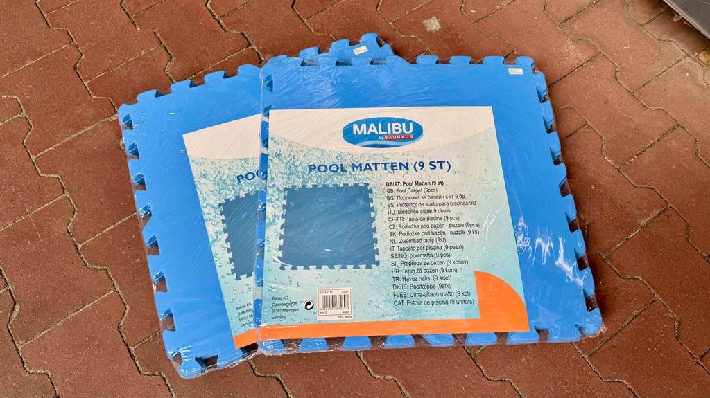 Zwei verpackte Pool-Unterlagen liegen zum Testen auf einem Steinfliesenboden.