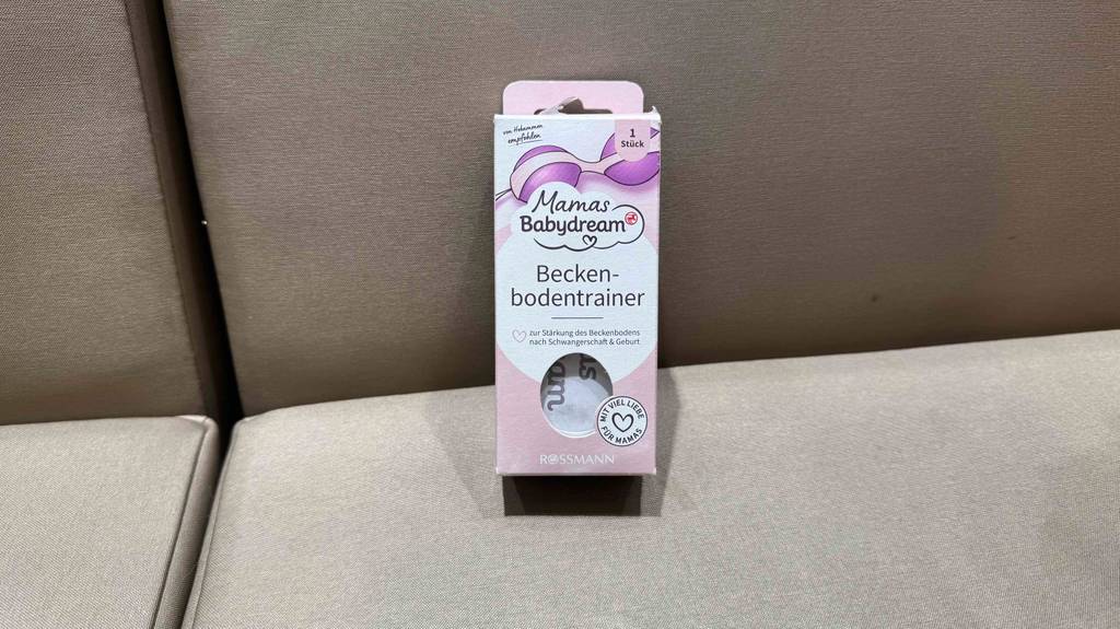 Getestet: Ein Beckenbodentrainer der Marke Mamas Babydream steht in der rosa Verpackung auf einem beigefarbenen Sofa.