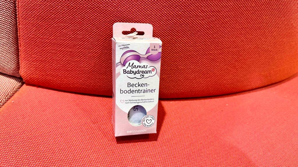 Beckenbodentrainer-Test: Ein Modell der Marke Mamas Babydream steht in der rosa Verpackung auf einem roten Sofa.