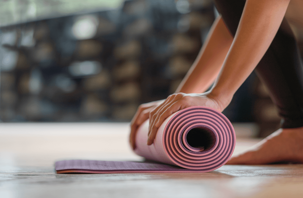 Manduka-Yogamatte-Test: Eine Frau rollt eine pinke Yogamatte zusammen. 