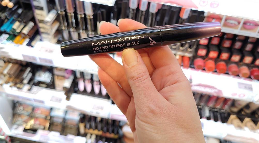 Eine Hand hält eine Manhattan-Mascara im Test vor ein Regal.