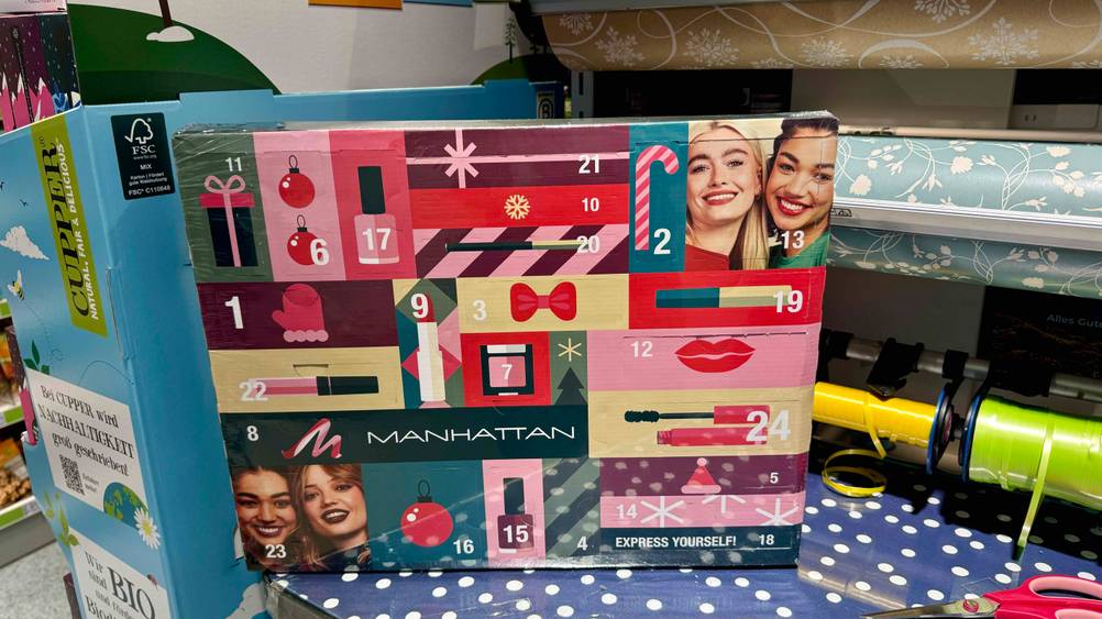 Ein Adventskalender für Frauen steht zum Testen zwischen mehreren Geschenkpapierrollen.