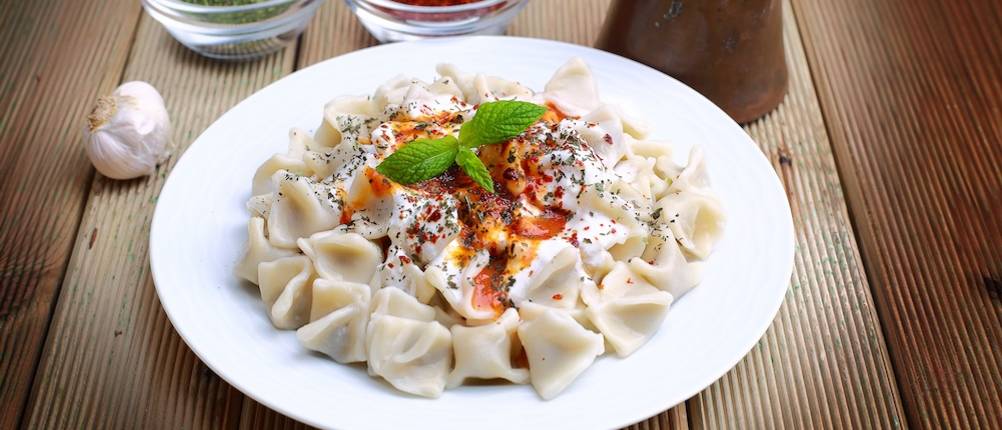 Frische Manti getestet: Ein weißer Teller mit frischen Manti und Gewürzen steht auf einem Holztisch.