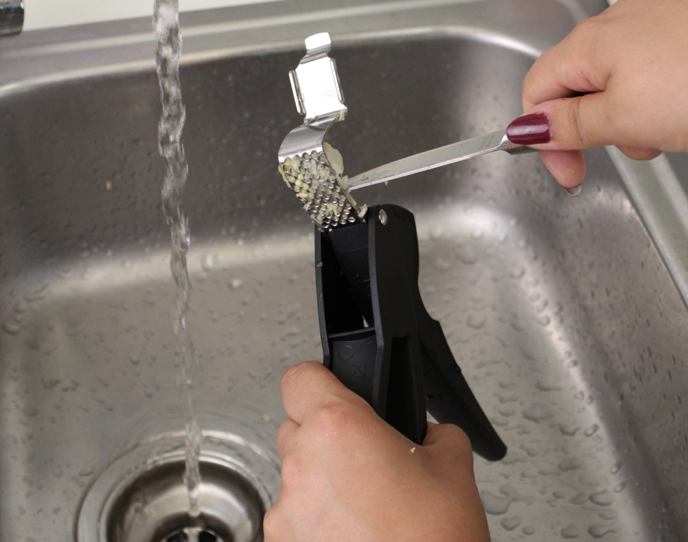 Reinigung einer Knoblauchpresse mit einem Messer und Wasser 