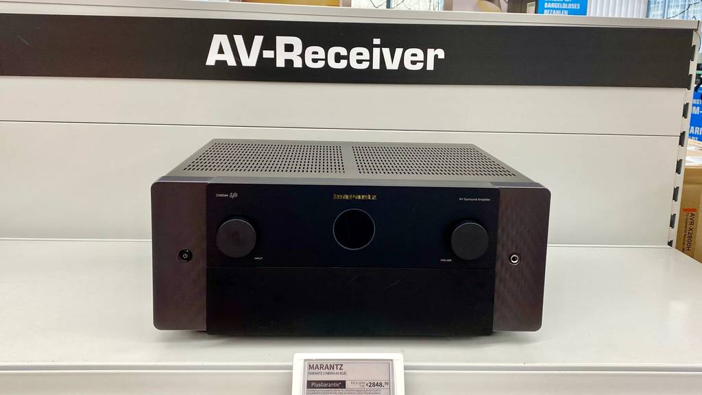 Vorderansicht eines getesteten AV-Receivers im schwarzen Design inklusive Preisschild auf einem weißen Verkaufsregal.