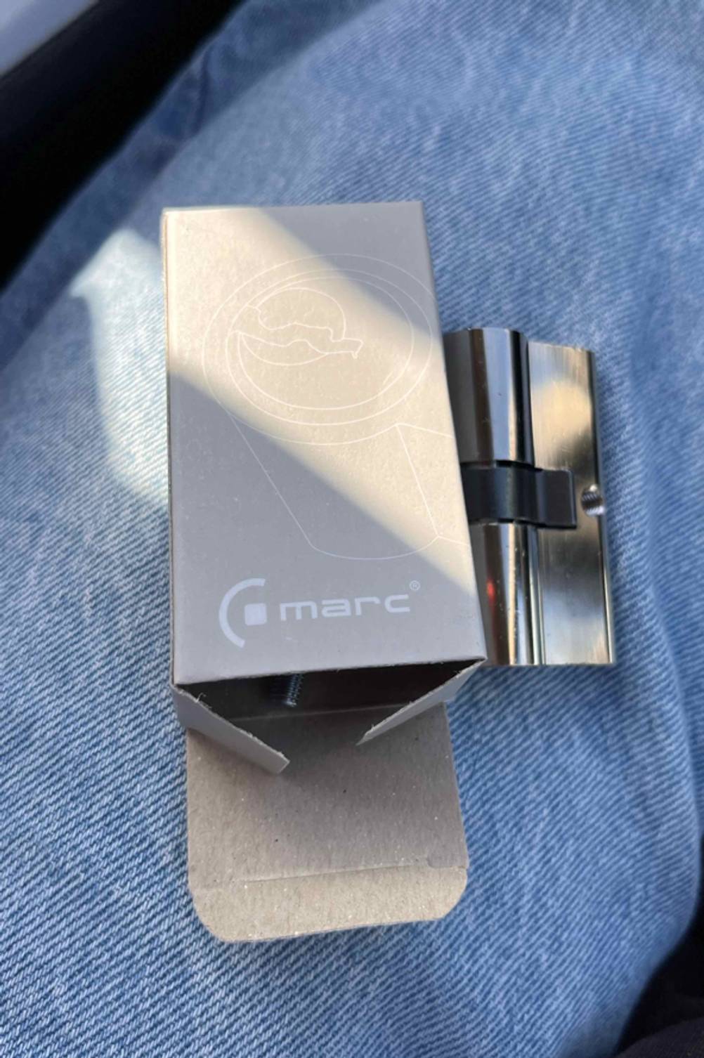 Knaufzylinder im Test der Marke Marc liegt ausgepackt neben seiner Originalverpackung auf einem Jeansuntergrund.