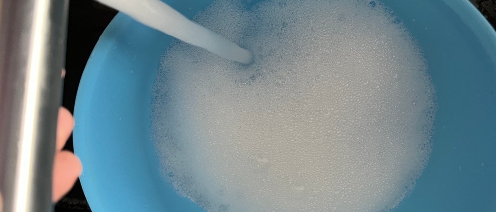 Es läuft Wasser in eine blaue Schüssel und Schaum entsteht.