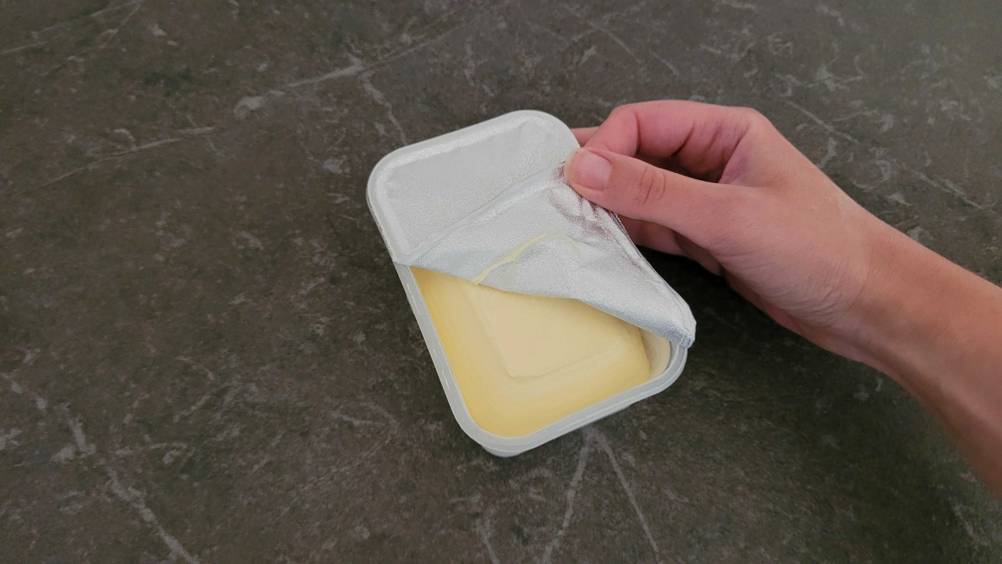 Im Test: Eine Hand öffnet das Frischesiegel auf einer Packung Margarine.