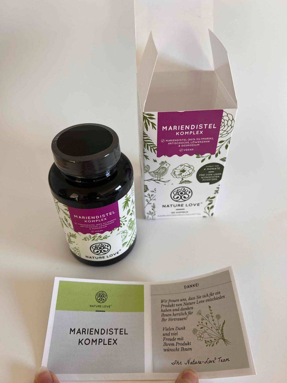 Neben der Originalverpackung steht eine Dose Mariendistel-Kapseln im Test, davor ein Beipackzettel.