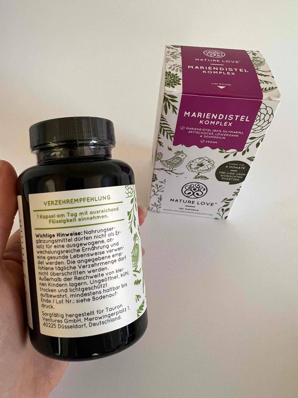 Eine Hand hält eine Kunststoffdose gefüllt mit getesteten Mariendistel-Kapseln.